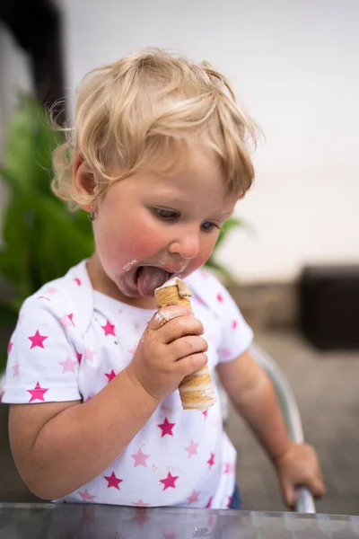 Маленькая девочка ест трубку со взбитыми сливками — стоковое фото