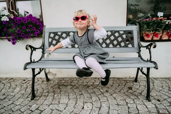 Kleines Mädchen mit Sonnenbrille sitzt auf Bank — Stockfoto