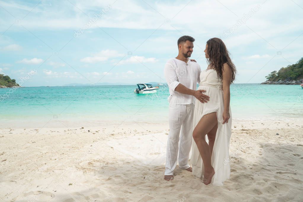 Attractive young couple on the tropical island. Beautiful woman and man wearing white clothes embracing each other and enjoying trpoical holidays vacation getaway