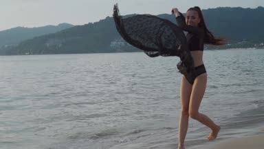 Siyah mayo onu tatil sahilde günbatımı sırasında zevk günbatımı / güzel kadında sırasında dantel eşarp ile oynarken sahilde güzel bir kadın. Kaygısız kadın siyah dantel kumaş - ağır çekimde video ile döşeme