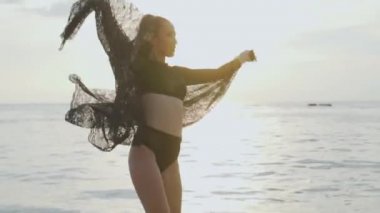 Siyah mayo onu tatil sahilde günbatımı sırasında zevk günbatımı / güzel kadında sırasında dantel eşarp ile oynarken sahilde güzel bir kadın. Kaygısız kadın siyah dantel kumaş - ağır çekimde video ile döşeme