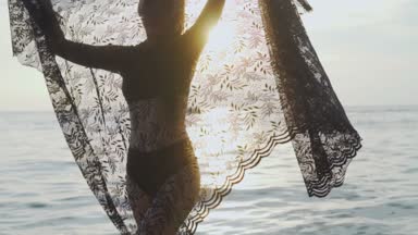 Siyah mayo onu tatil sahilde günbatımı sırasında zevk günbatımı / güzel kadında sırasında dantel eşarp ile oynarken sahilde güzel bir kadın. Kaygısız kadın siyah dantel kumaş - ağır çekimde video ile döşeme