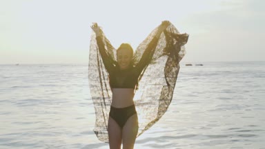 Siyah mayo onu tatil sahilde günbatımı sırasında zevk günbatımı / güzel kadında sırasında dantel eşarp ile oynarken sahilde güzel bir kadın. Kaygısız kadın siyah dantel kumaş - ağır çekimde video ile döşeme