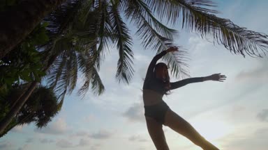 Güzel kadın kumsalda dans / alt görünümü içinde siyah mayo palmiye ağacı ve gökyüzü arka plan - ağır çekimde video üzerinden günbatımı sırasında kumsalda dans güzel kadın