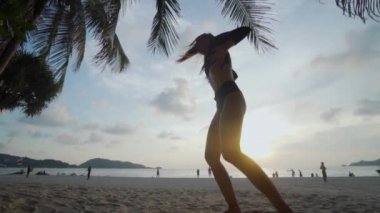 Güzel kadın kumsalda dans / alt görünümü içinde siyah mayo palmiye ağacı ve gökyüzü arka plan - ağır çekimde video üzerinden günbatımı sırasında kumsalda dans güzel kadın