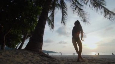 Güzel kadın kumsalda dans / alt görünümü içinde siyah mayo palmiye ağacı ve gökyüzü arka plan - ağır çekimde video üzerinden günbatımı sırasında kumsalda dans güzel kadın