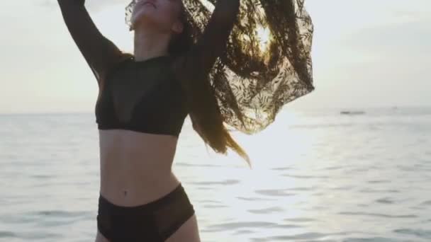 美丽的女人在海滩上玩花边围巾在日落 美丽的女人在黑色泳装享受她在海滩上的假期在日落期间 无忧无虑的妇女铺设黑色花边织物 视频慢动作 — 图库视频影像