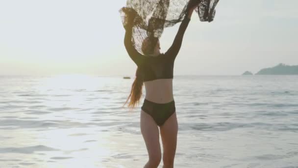 美丽的女人在海滩上玩花边围巾在日落 美丽的女人在黑色泳装享受她在海滩上的假期在日落期间 无忧无虑的妇女铺设黑色花边织物 视频慢动作 — 图库视频影像