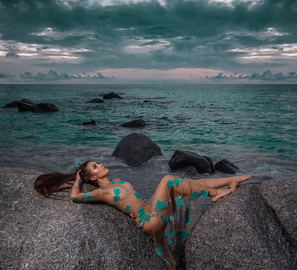 謎の女は美しい海と曇り夕焼け空背景を岩の上敷設ロング ドレス — ストック写真