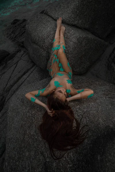 美丽的神秘女人穿上长裙躺在海面上的岩石和多云的日落天空背景 — 图库照片