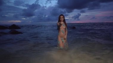 Sahilde günbatımı/güzel gizemli kadın uzun elbiseli deniz suyu bulutlu gün batımı gökyüzü arka plan üzerinde yürüme sırasında gizemli güzellik