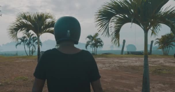 曇り早朝スローモーションのビデオの中に美しい熱帯マウンテン ビューに彼のチョッパー バイクにウォーキング クールな旅行の無料バイク ライダー 背面図 — ストック動画