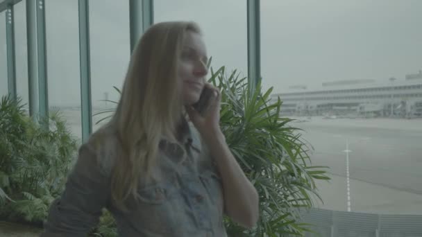 空港で携帯電話を持つ女性 女性が空港に携帯電話で話しています 女の子は 空港の待合室でフライトを待っています — ストック動画