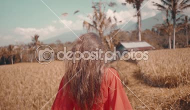 Güzel kadını pirinç tarla / arkadan görünüşü pirinç alan - ağır çekimde video boyunca çalışan kırmızı şeffaf elbiseli güzel genç kadın