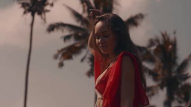 Güzel kadın pirinç tarlaları / güzel tropikal bulutlu gökyüzü arka plan - ağır çekimde video üzerinde pirinç alanında poz kırmızı şeffaf elbiseli Genç kadın