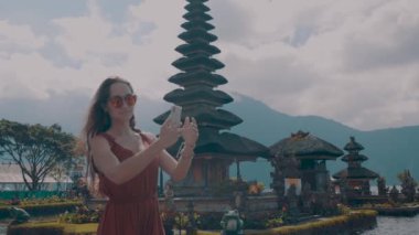 Genç kadın turist onu tatil Adası Bali, Endonezya - video yavaş hareket üzerinde Ulun Danu Batur Tapınağı'nda cep telefonu ile selfie fotoğraf yapıyor sahiptir