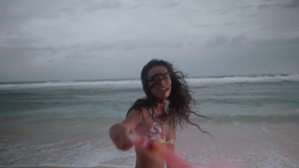 美丽的快乐的女孩玩彩色烟雾 而站在海滩上空的海洋和多云的天空背景 视频慢动作 — 图库视频影像