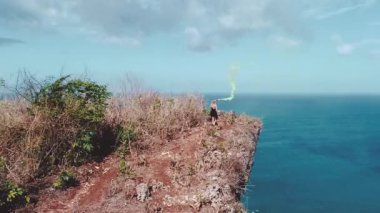 Güzel kızın muhteşem okyanus ve bulutlu gökyüzü görünümü - ağır çekimde video uçurumun altındaki renkli duman ile oynamak hava dron vurdu