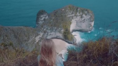 Arkadan görünüşü güzel Kelingking Beach kayalıklarla arka planda Nusa Penida, Bali, Endonezya üzerinden cliff üzerinde oturan kız