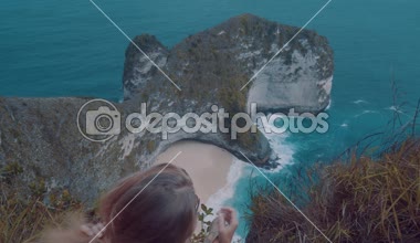 Arkadan görünüşü güzel Kelingking Beach kayalıklarla arka planda Nusa Penida, Bali, Endonezya üzerinden cliff üzerinde oturan kız