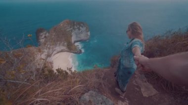 Cliff üzerinde duran ve güzel Kelingking Beach kayalıklarla arka planda Nusa Penida, Bali, Endonezya üzerinden erkek arkadaşının elini tutarak kız
