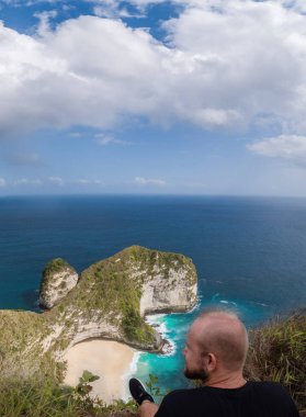 Güzel Kelingking Beach kayalıklarla arka planda Nusa Penida, Bali, Endonezya üzerinden cliff üzerinde oturan adam arkadan görünüm