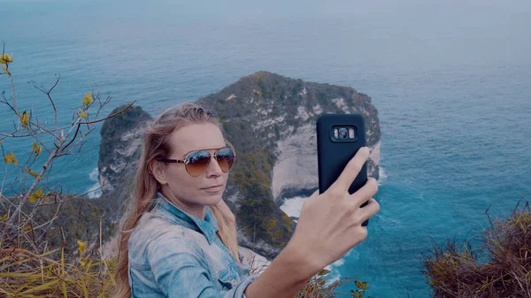 ペニダ島 バリ島 インドネシアの驚くべき Kelingking ビーチの崖の上に立っている間 Selfie 写真をやってきれいな女の子の旅行者 — ストック写真