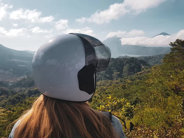 Back view of woman tourist in helmet admire beautiful view of Batur lake and Mount Agung in Bali, Indonesia