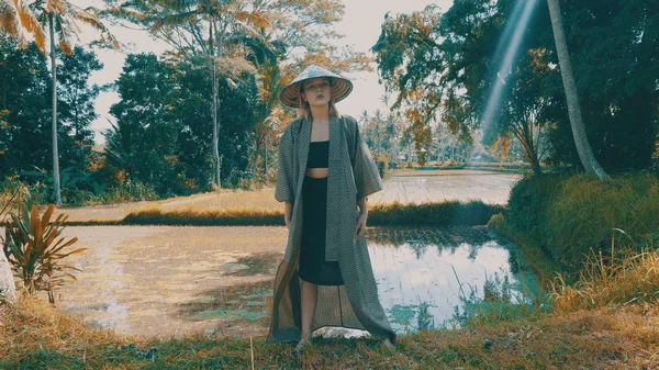 着物と熱帯イネでポーズをとる伝統的なバリの麦わら帽子で美しいファッションの少女はフィールド テラスです 屋外のスタイリッシュな流行に敏感な女性の肖像画 — ストック写真