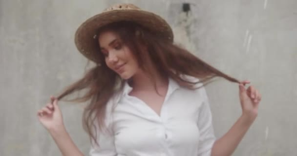 白いドレスと灰色のコンクリート壁で分離された麦わら帽子で微笑んでいる女の子のファッション美容肖像画 — ストック動画