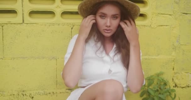 白いドレスと麦わら帽子の明るい黄色の壁で分離で微笑んでいる女の子のファッション美容肖像画 — ストック動画
