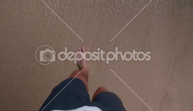 Kumlu sahilde yürüyen adam. Closeup erkeğin ayaklarınızı yıkadım dalgalar tarafından deniz - ateş ilk kişi görünümü