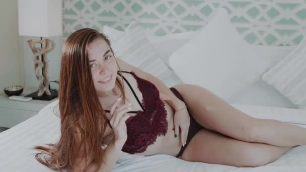 モダンな内装のヴィラの家寝室 スローモーションのビデオのベッドでポーズのランジェリーの美しい赤い髪の少女 — ストック動画