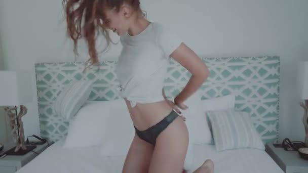 美丽的金发女孩在T恤和内裤跳舞在床在现代装饰别墅房子卧室 — 图库视频影像