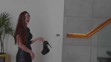 Yüksek topuklu lüks modern iç - ağır çekimde video içinde yürürken elinde tutan şık elbiseli güzel kızıl saçlı kız