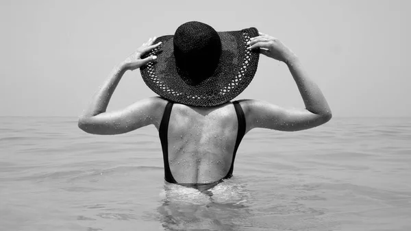 海の中で女性の後ろ姿 水着と麦わら帽子彼女の休日 黒と白の写真を楽しんで身に着けている女の子 — ストック写真