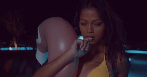 黄色ビキニの夜 スローモーションのビデオの間に屋外スイミング プールでピンクの膨脹可能なフラミンゴのポーズで美しい女性 — ストック動画