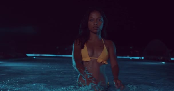 スローモーションのビデオの間に屋外スイミング プールの水をはねながらカメラに探している黄色のビキニで美しい女性 — ストック動画
