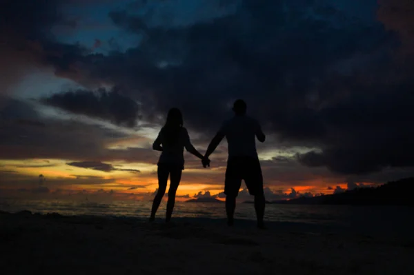 海の上のビーチで手をつないで 美しい金の夕日の空の背景にカップル ロマンチックな旅行の休日の概念 — ストック写真