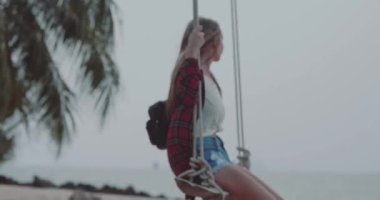 Bulutlu ve rüzgarlı sabah sırasında plajda Swing zevk kadının yan görünümü