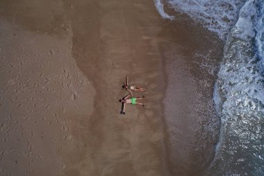 Okyanus ayakın kumlu plajda yatarken el ele tutuşan çiftin havadan üst görünümü. Yaz tatili konsepti 