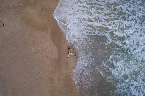 Okyanus ayakın kumlu plajda yatarken el ele tutuşan çiftin havadan üst görünümü. Yaz tatili konsepti 