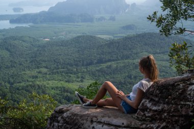 Kadın taveler uçurumda oturan ve dağlar ve vadi ile güzel manzara bakıyor 