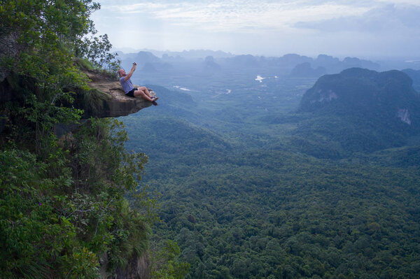Вид с воздуха на человека дрона оператора на краю скалы над красивыми зелеными горами и небо фон
