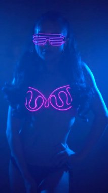 Puslu stüdyo gece kulübünde neon yanıp sönen pembe sütyen ve gözlük giyen Parti şehvetli kadın - yavaş hareket dikey video