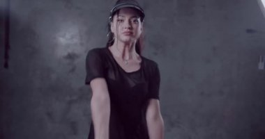 Siyah giyen şehvetli kadın t-shirt, iç çamaşırı ve güneş vizörü gri beton duvarlar ile stüdyoda dans ile görmek - yavaş hareket video