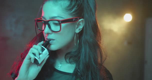 ネオンカラーライトで電子タバコを吸うゴージャスなブルネットの女性 スローモーションでビデオ — ストック動画