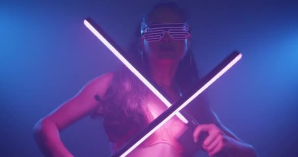 ネオンの点滅ピンクのブラジャーとメガネを身に着けているパーティー官能的な女性は 曇ったスタジオのナイトクラブで光る光の棒で踊る スローモーションでビデオ — ストック動画