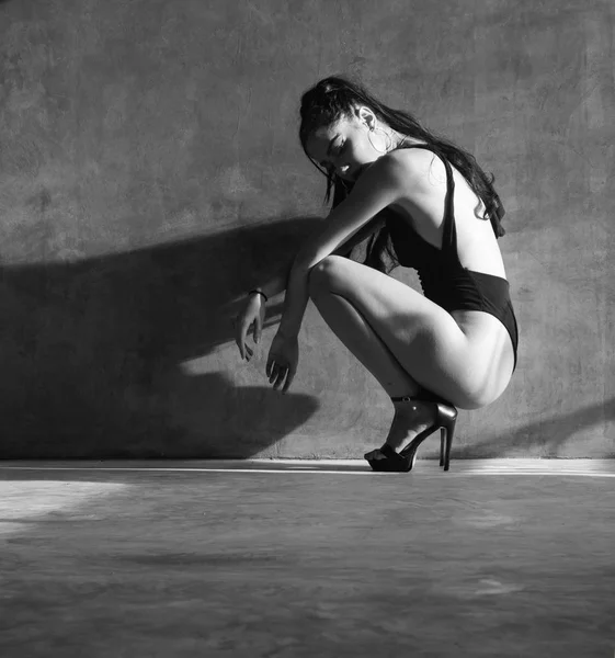 黒いボディスーツの美しい官能的な女性は 灰色のコンクリートの壁の背景の上に美しい日光とスタジオでポーズ 黒と白の写真 — ストック写真