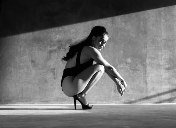 黒いボディスーツの美しい官能的な女性は 灰色のコンクリートの壁の背景の上に美しい日光とスタジオでポーズ 黒と白の写真 — ストック写真